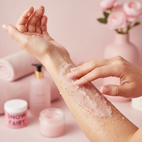  "Femme appliquant gommage corporel exfoliant à la fraise Snow Fairy sur son bras dans une salle de bain lumineuse"